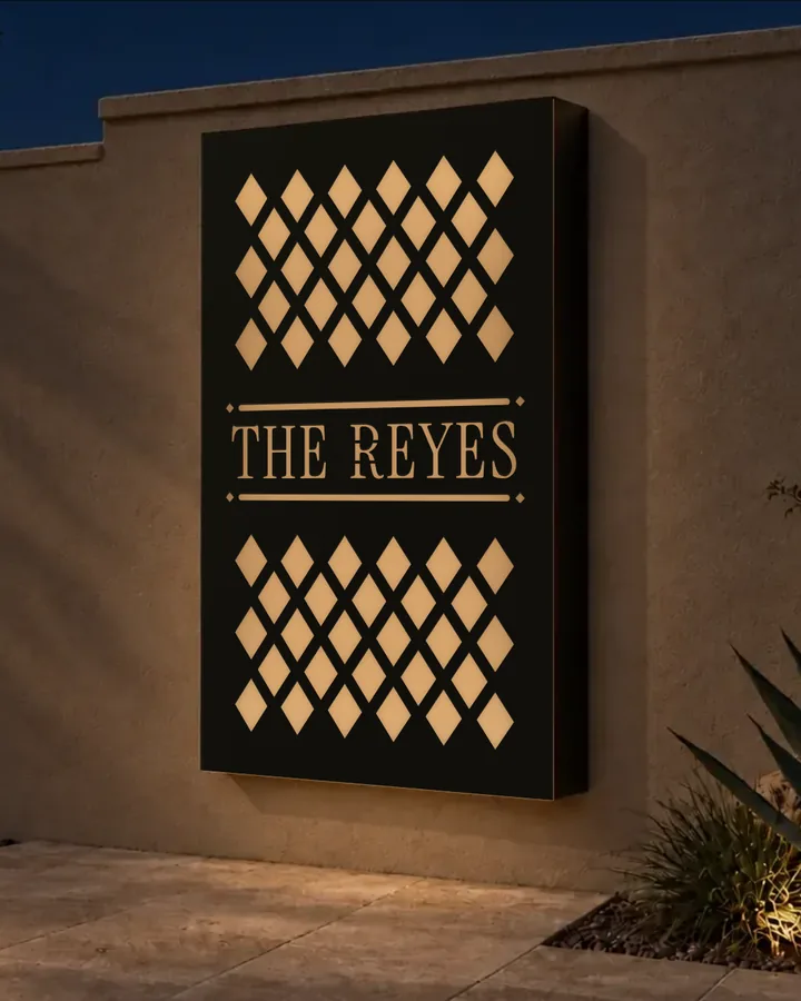 A Trelace Frame on a stucco courtyard wall at night, its screen cut with the family name The Reyes between two rules and lit from within